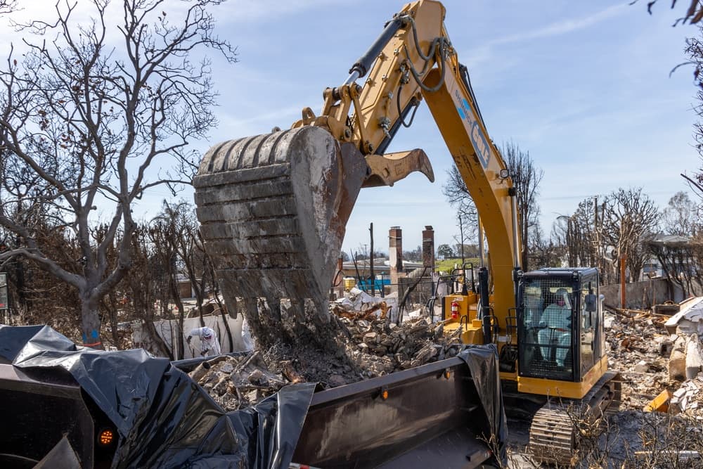 An excavator clearing fire debris from a destroyed residential lot during the federal Palisades cleanup